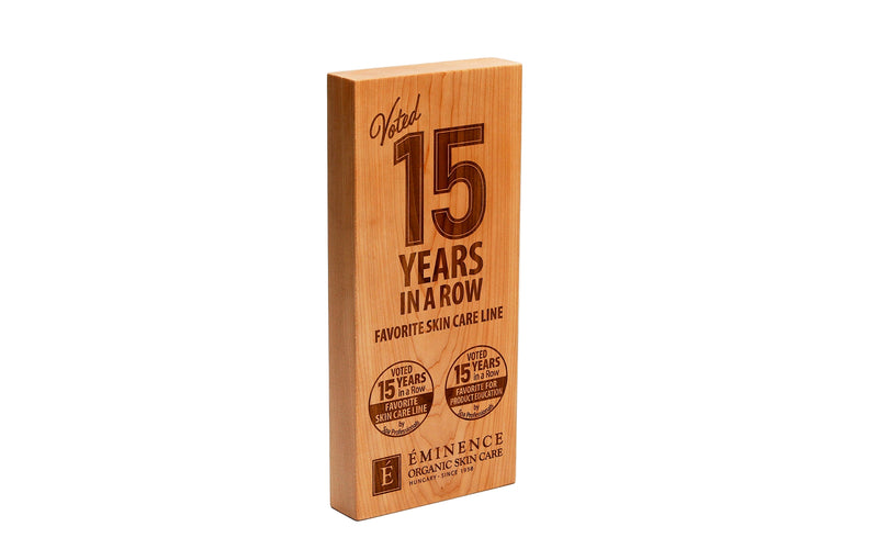 Wooden box with engraved text celebrating Eminence Organic Skin Care's 15 years in business on a white background.